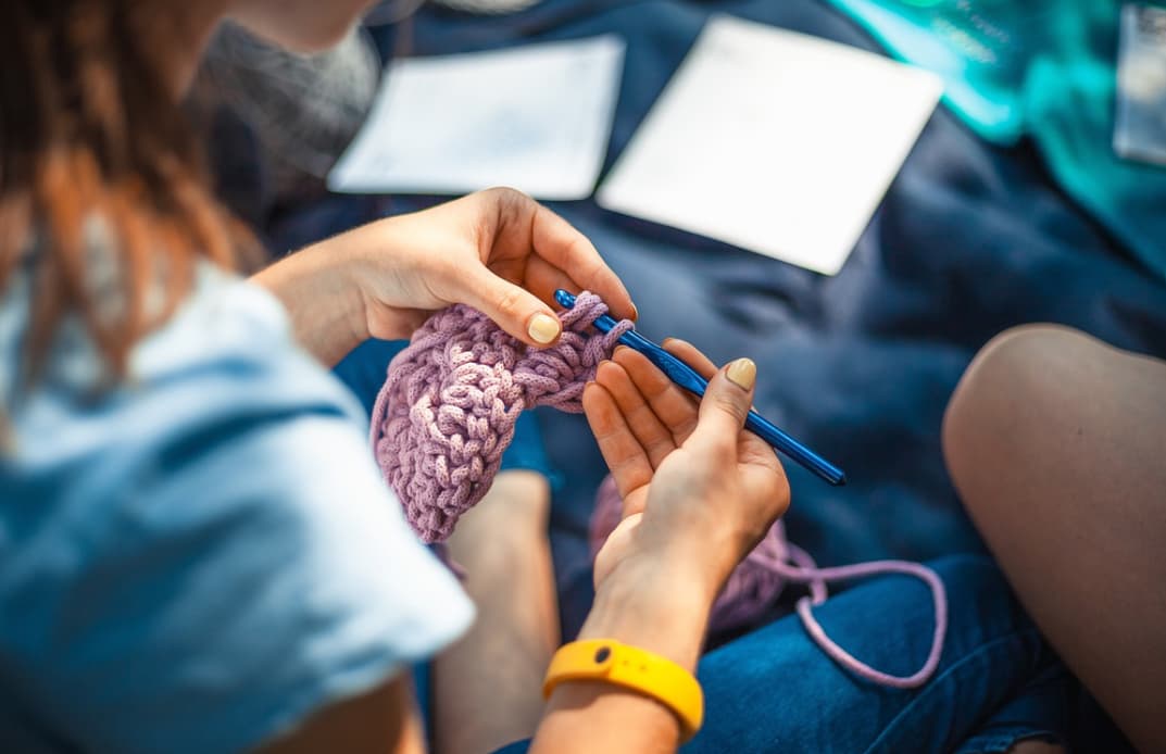 hands hold knitting needles and pink yarn