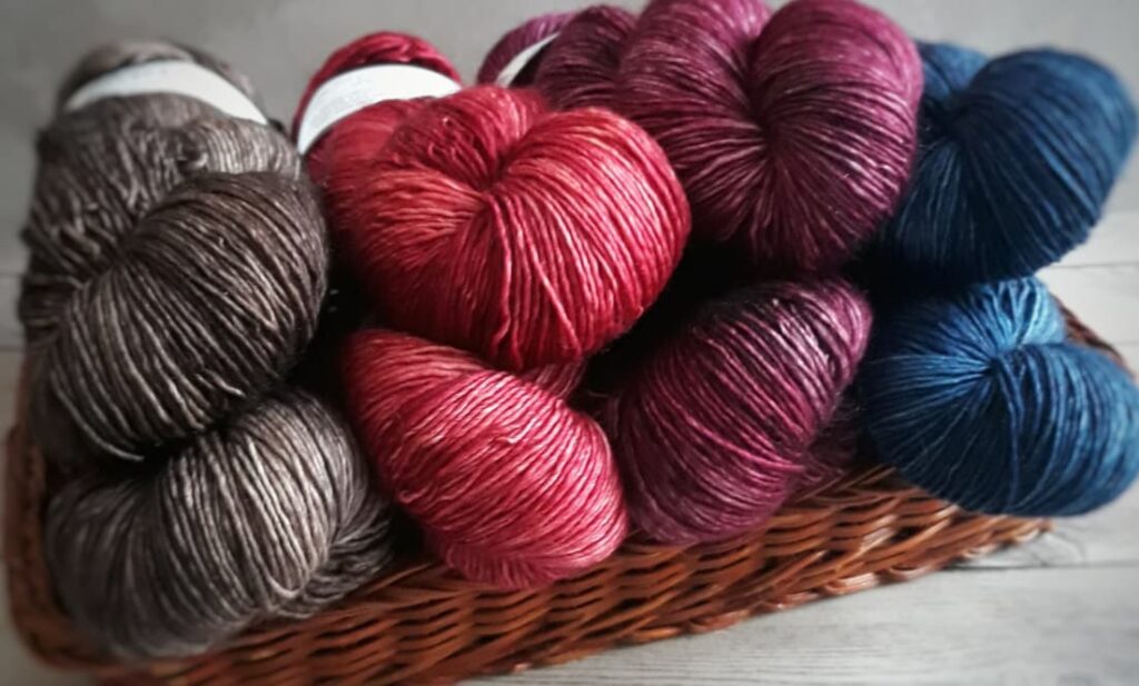 A basket filled with skeins of yarn in shades of brown, red, and blue, on a dark wooden surface