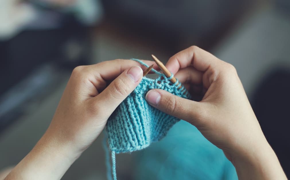 hands hold knitting needles and blue yarn