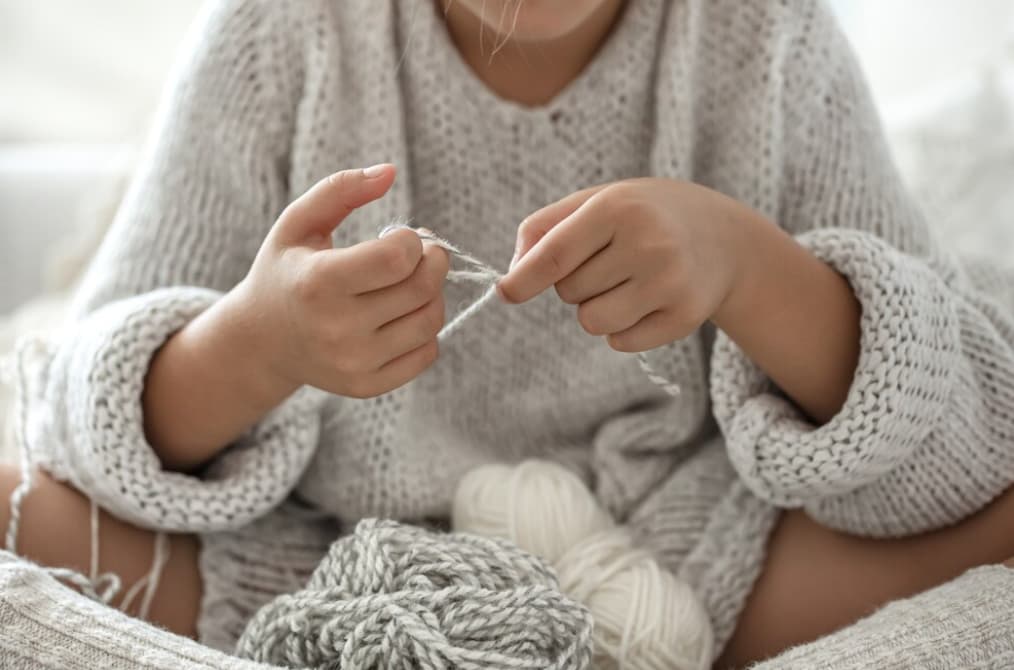 girl in a gray sweater sitting on the sofa and knitting