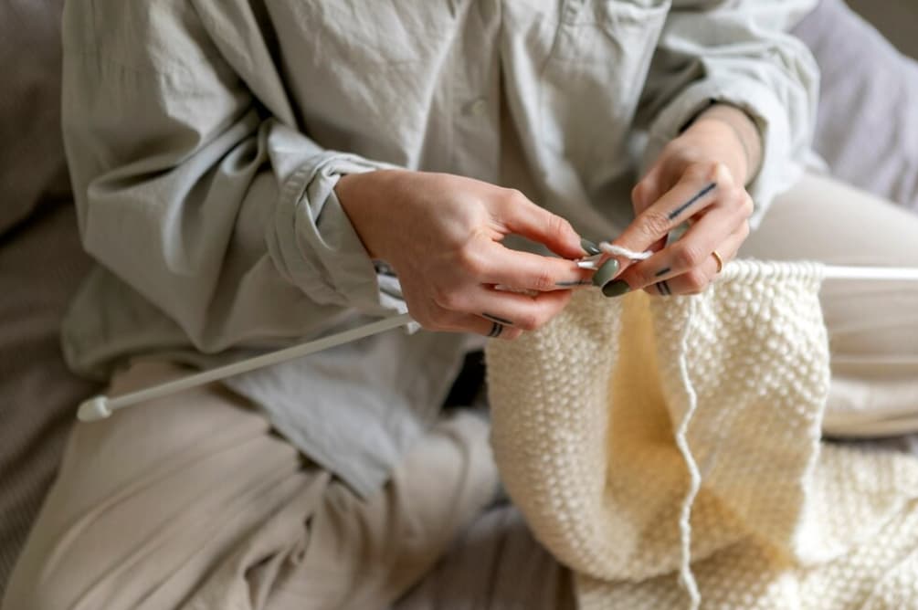 A person knitting with white yarn and large needles, focused on their work