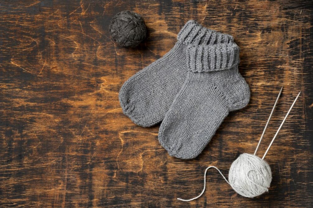 two gray socks, white and black yarns and needles on the wooden table