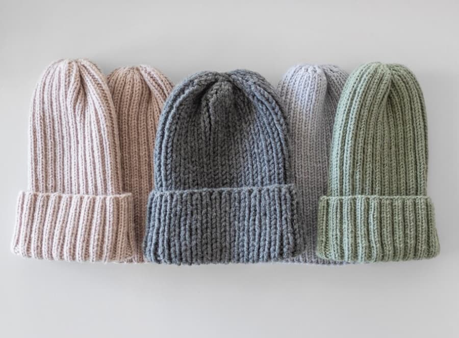 Four knitted beanies in soft pastel colors lined up on a white surface