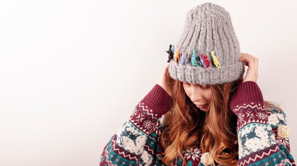 A woman covers her face with a grey beanie adorned with small figures