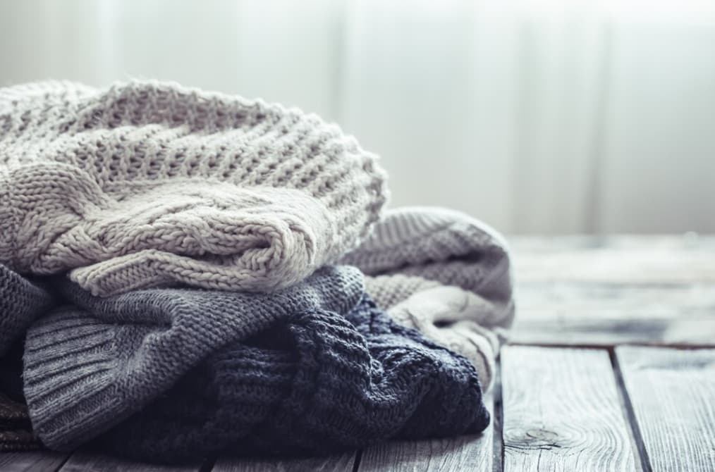 A stack of knitted sweaters in neutral colors on a wooden surface