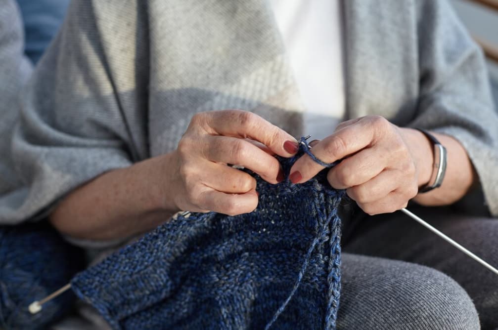 Close-up of hands knitting with blue yarn and metal needles