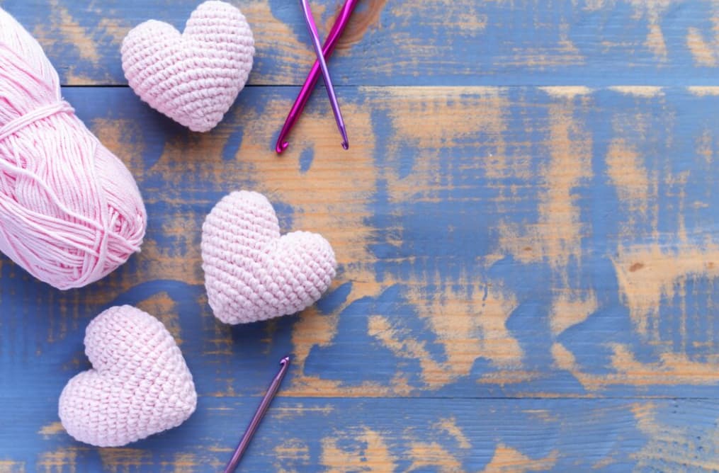 top view of handmade knitted three pink hearts with a pink ball of yarn