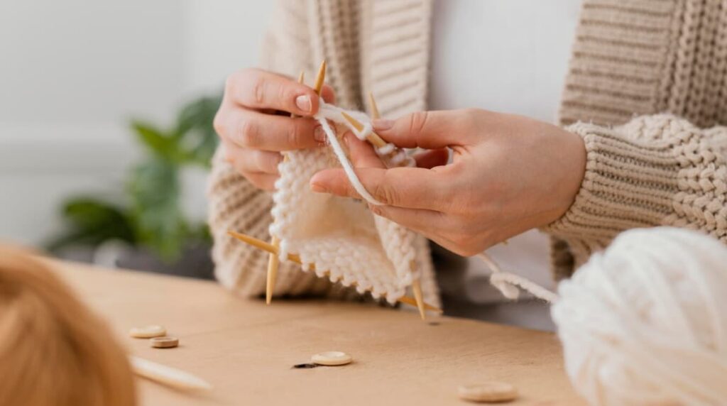 Close-up of hands knitting with white yarn and wooden needles