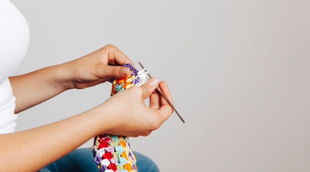 Hands knitting a colorful piece with metal needles