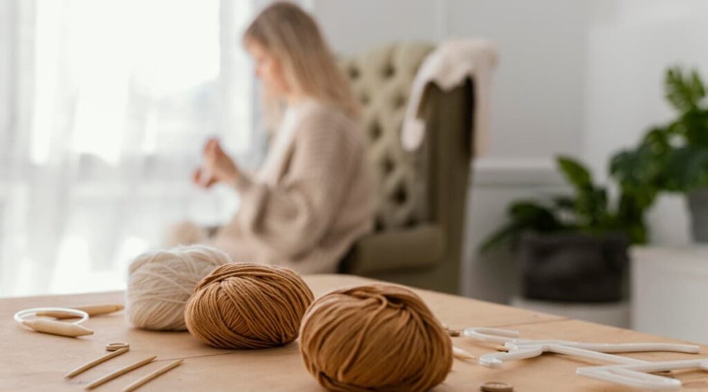 Yarn balls and knitting tools on a table, with a person in the background