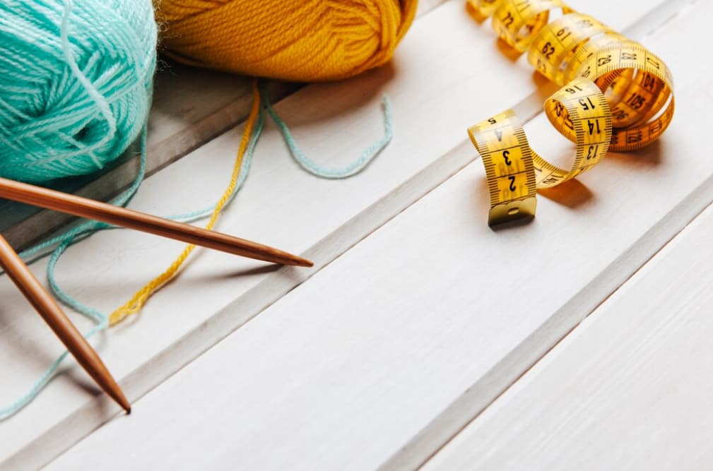 Knitting needles, yarn, and a measuring tape on a wooden surface