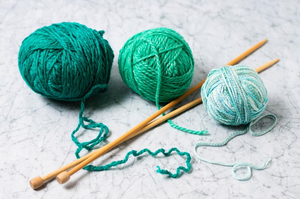 Varied green yarn balls and needles on a textured surface