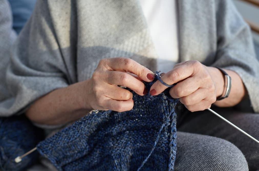 A person's hands knitting with blue yarn, close-up view