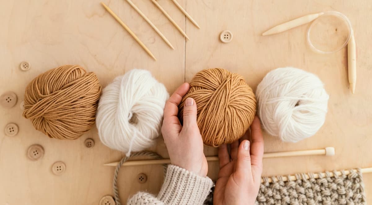 Hands holding yarn balls with knitting needles on a wooden surface