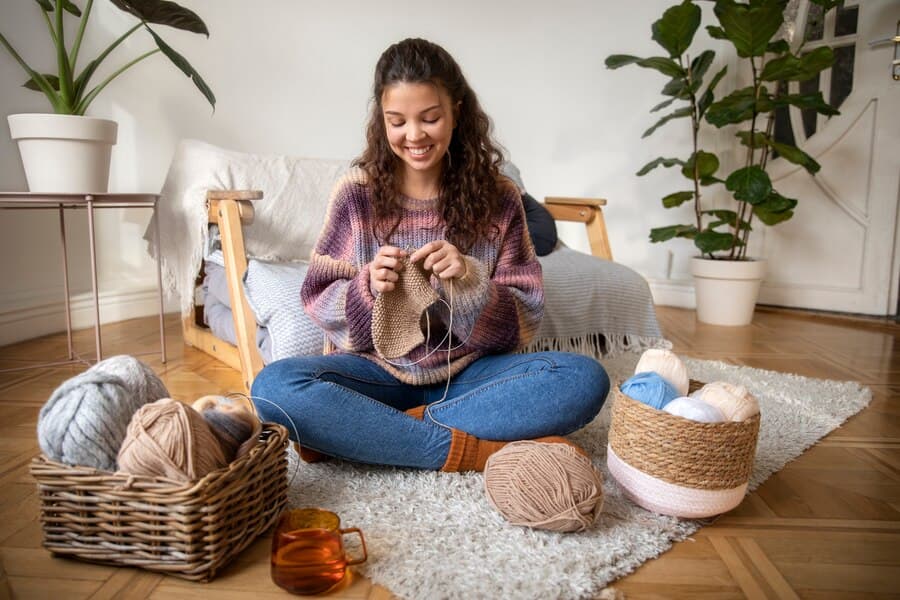 The girl is sitting on the floor and knitting